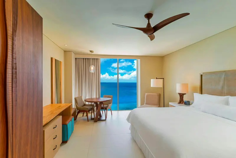 Chambre lumineuse avec un lit blanc et une vue sur la mer.