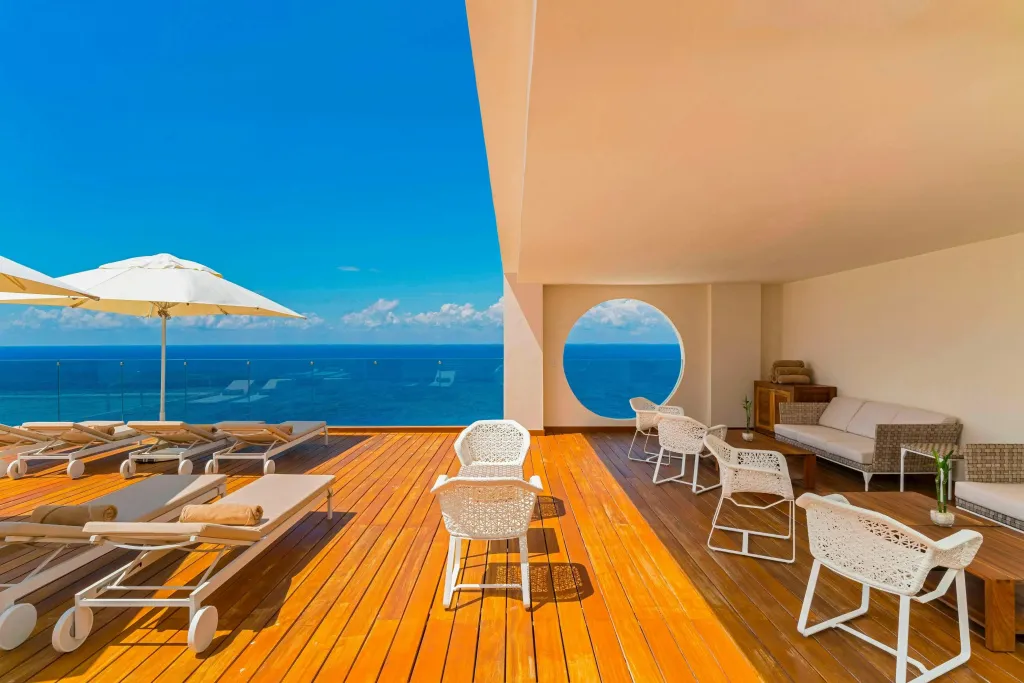 Terrasse en bois avec transats et mobilier de détente face à la mer.