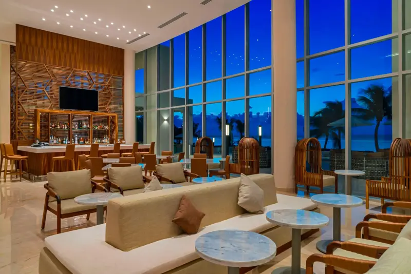 Un espace de détente intérieur avec des canapés et un bar en arrière-plan, donnant sur une vue nocturne sur la mer.