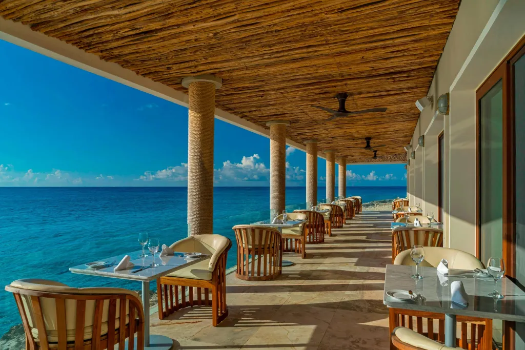 Terrasse ombragée avec tables dressées face à la mer turquoise.