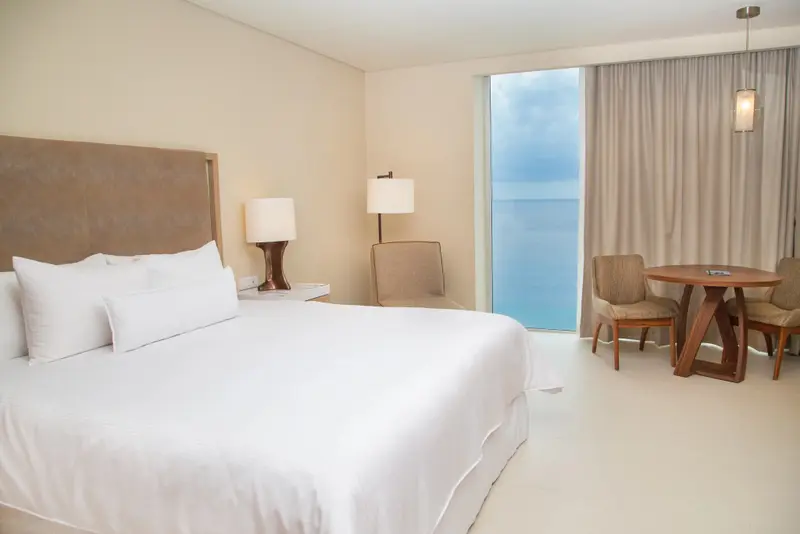 Une chambre lumineuse avec un grand lit et un coin repas près d'une fenêtre.