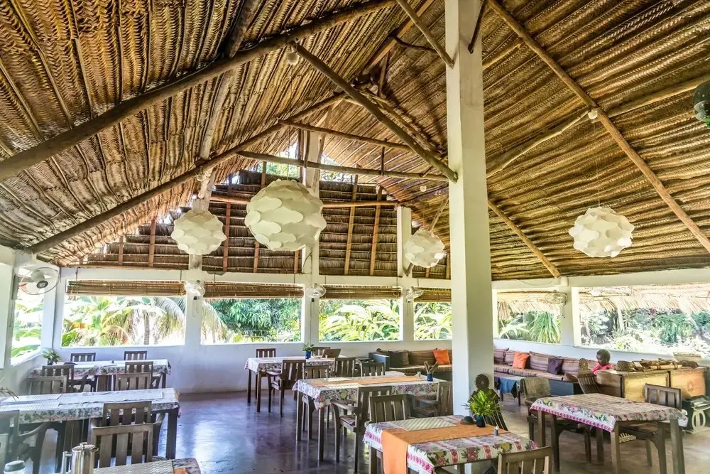 Une salle de restaurant spacieuse avec un toit de chaume et des tables dressées.