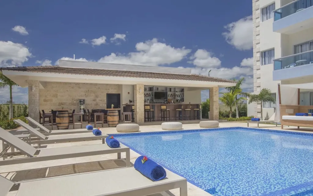 Une piscine turquoise bordée de transats blancs sous un ciel nuageux.