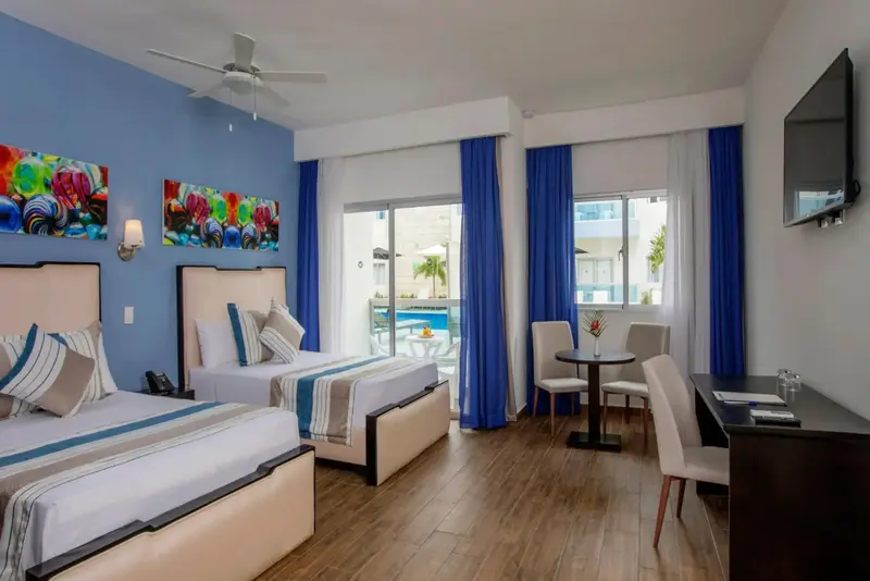 Chambre lumineuse avec deux lits et un coin repas près d'une fenêtre.
