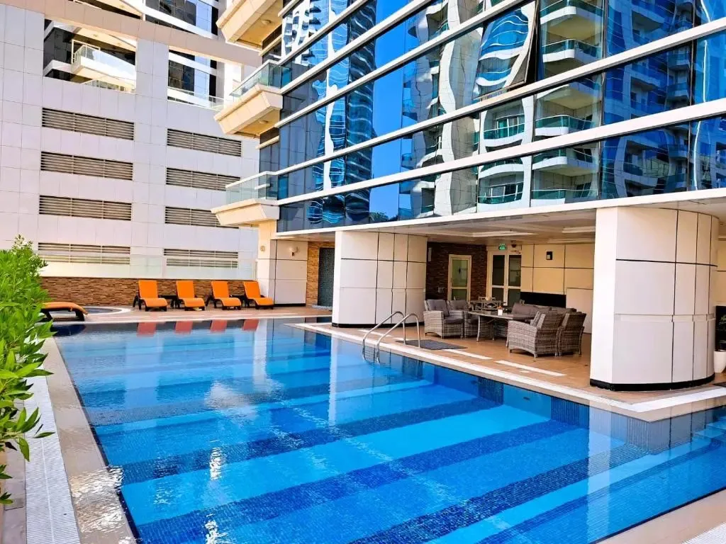 Une piscine rectangulaire bleue avec des transats orange et des meubles de jardin.