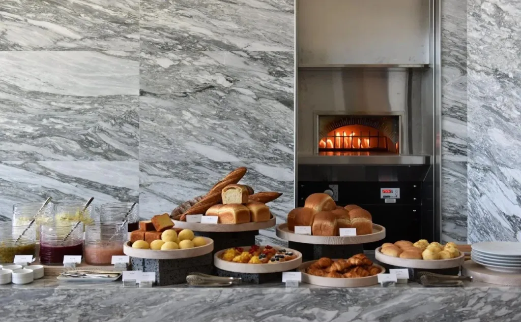 Un buffet propose une variété de pains et de pâtisseries devant un four à pain.