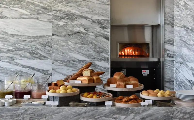 Un buffet propose une variété de pains et de pâtisseries devant un four à pain.