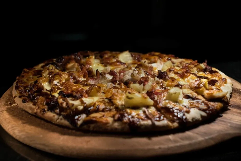Une pizza garnie de jambon et d'ananas est présentée sur une planche à découper en bois.