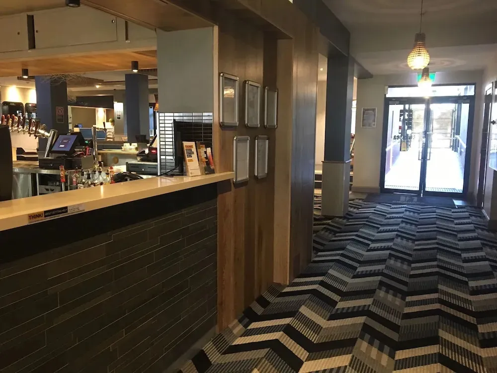 Un comptoir de bar en bois sombre avec des bouteilles et des verres derrière.