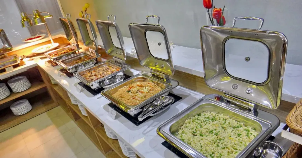 Un buffet propose une variété de plats chauds dans des récipients en acier inoxydable.