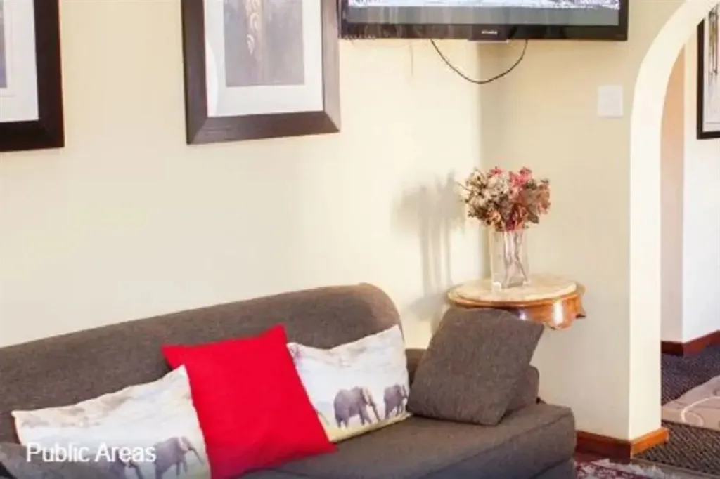 Un canapé gris avec des coussins colorés est placé devant un mur beige orné de tableaux.