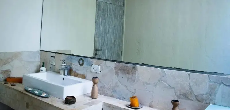 Un lavabo blanc est installé sur un meuble en pierre claire devant un grand miroir.