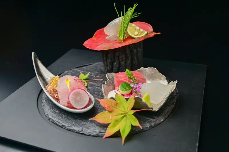 Présentation raffinée de tranches de poisson cru et de légumes sur une ardoise noire.