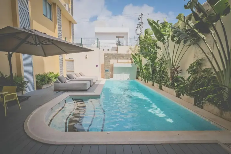 Une piscine rectangulaire turquoise est entourée d'un espace aménagé avec des transats et des plantes.