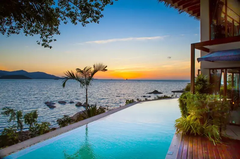 Une piscine à débordement surplombe la mer au coucher du soleil.
