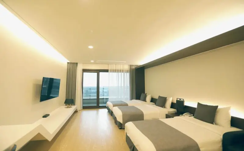 Une chambre lumineuse avec trois lits simples et un accès à une terrasse.