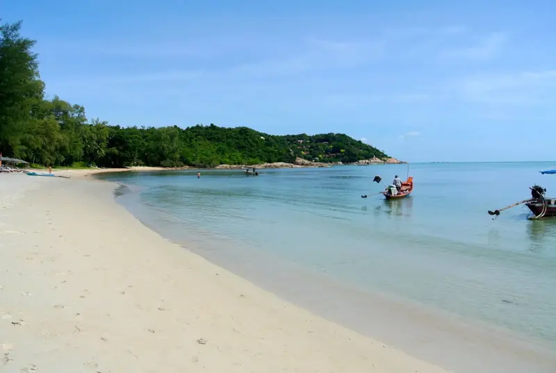 Une plage de sable blanc borde une eau turquoise sous un ciel bleu.