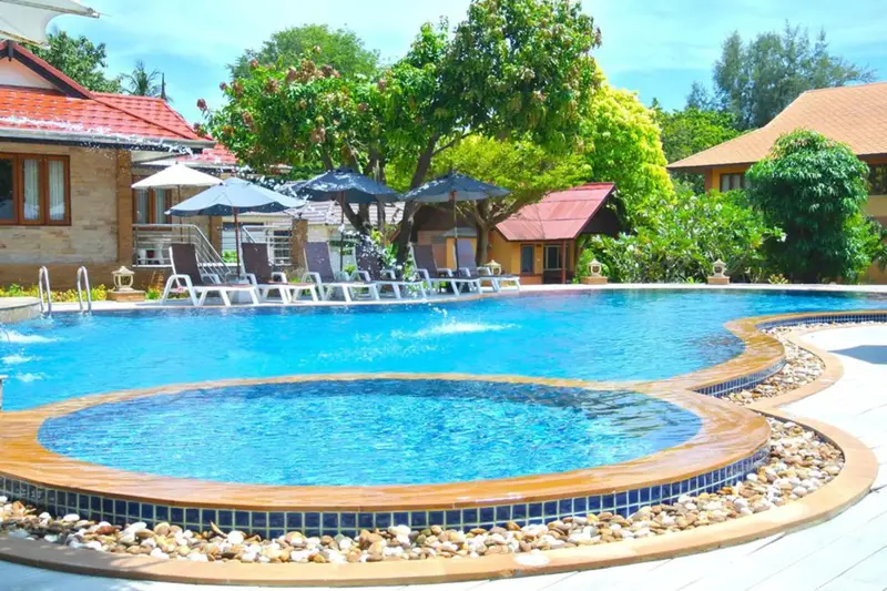 Piscine bleue avec des transats et des parasols dans un jardin tropical.