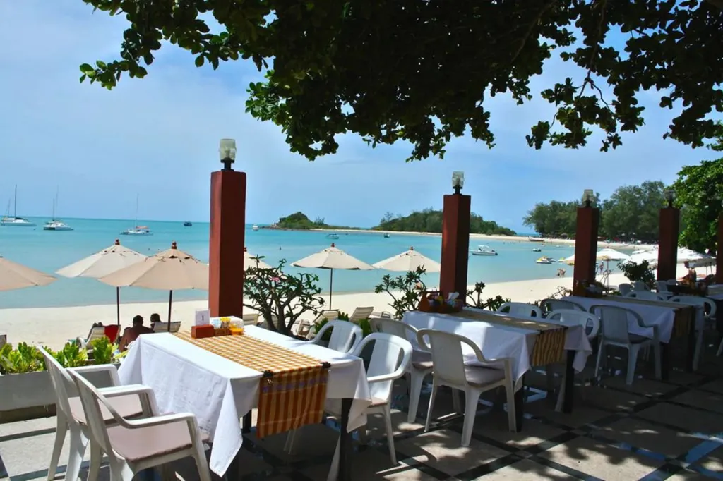 Une terrasse ombragée avec des tables dressées face à une plage et à la mer.