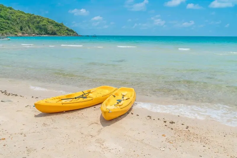 Deux kayaks jaunes reposent sur une plage de sable fin face à une mer turquoise.