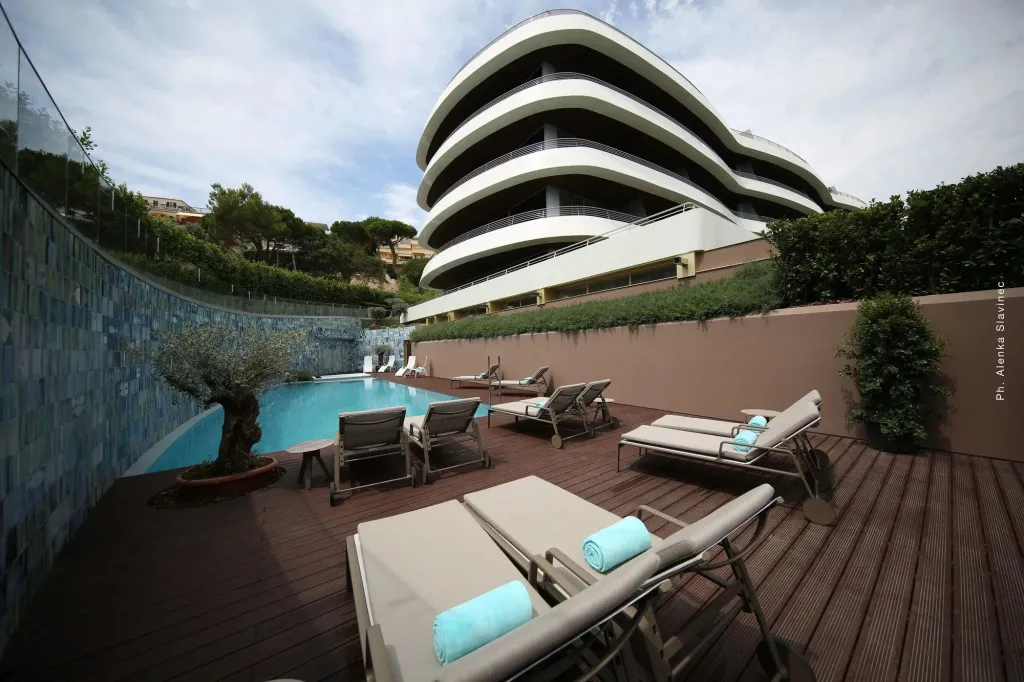 Terrasse avec transats et piscine au pied d'un bâtiment moderne.