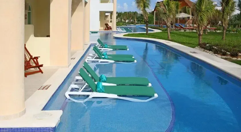 Transats verts alignés au bord d'une piscine sinueuse.