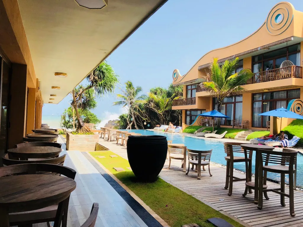 Terrasse ombragée donnant sur une piscine et la mer.