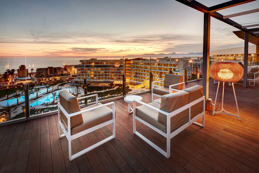 Terrasse aménagée avec des fauteuils et une vue sur la mer au coucher du soleil.