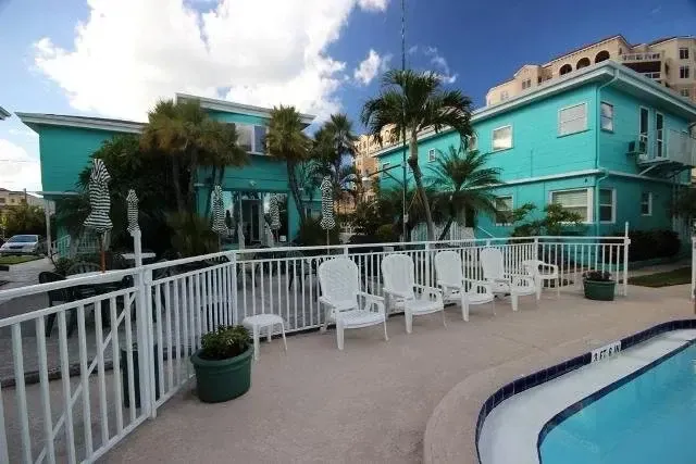 Bâtiment turquoise avec des chaises longues blanches près d'une piscine.