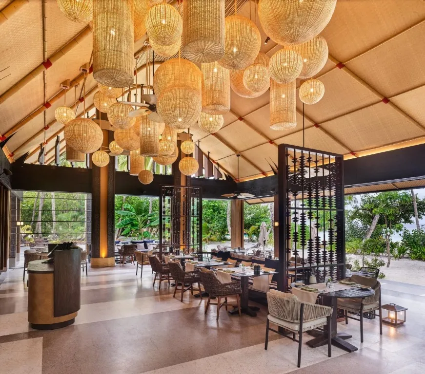 Une salle lumineuse avec de nombreuses suspensions en rotin et des tables disposées pour les repas.