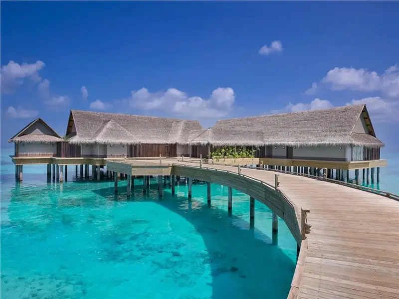 Des bungalows sur pilotis s'étendent sur une eau turquoise sous un ciel bleu nuageux.