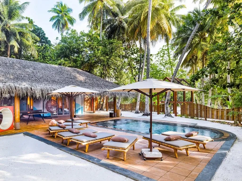 Transats et parasols bordent une piscine dans un cadre tropical.