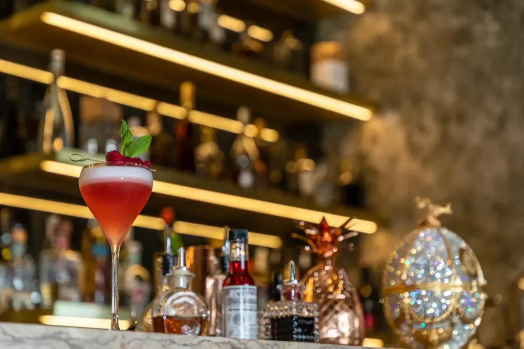 Un cocktail rose est servi dans un verre à martini sur un comptoir de bar éclairé.