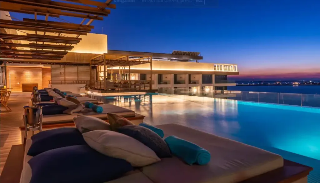 Transats et piscine à débordement illuminés au crépuscule.