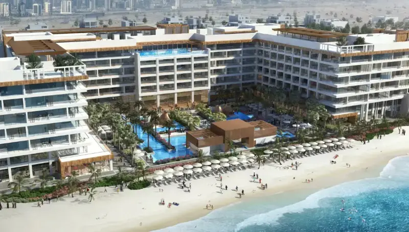 Vue aérienne d'un complexe hôtelier blanc avec des piscines et une plage de sable fin.