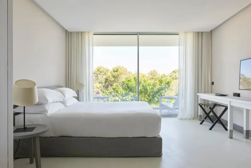 Une chambre lumineuse avec un grand lit et une vue sur la végétation.