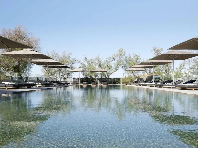 Une piscine rectangulaire bordée de transats sous des parasols.