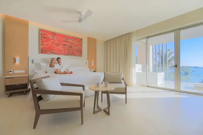 Une chambre lumineuse avec un grand lit et un coin salon donnant sur une vue mer.
