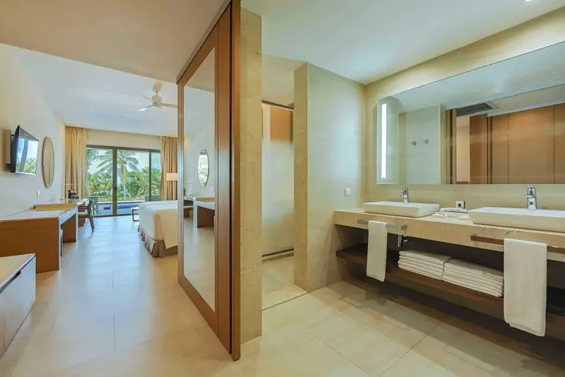 Une chambre lumineuse s'ouvre sur une salle de bain moderne avec deux vasques.