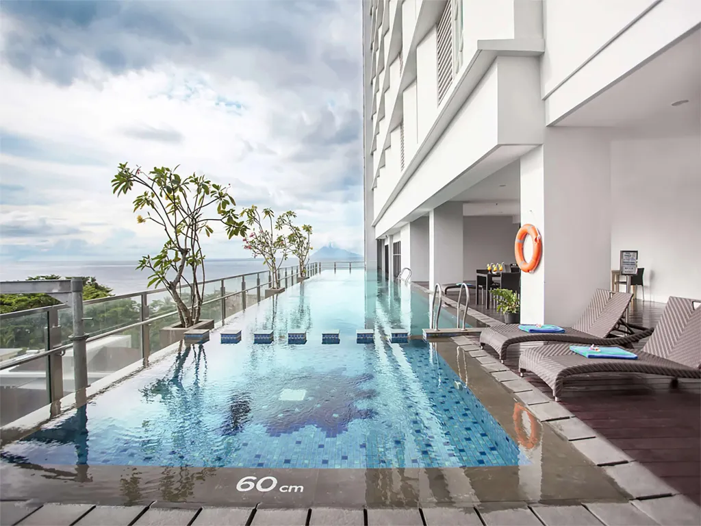 Une piscine rectangulaire bordée de transats offre une vue sur la mer.