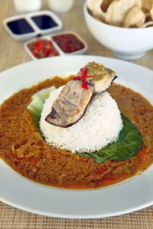 Un plat de riz accompagné d'une sauce épicée et d'un poisson grillé est présenté dans une assiette.