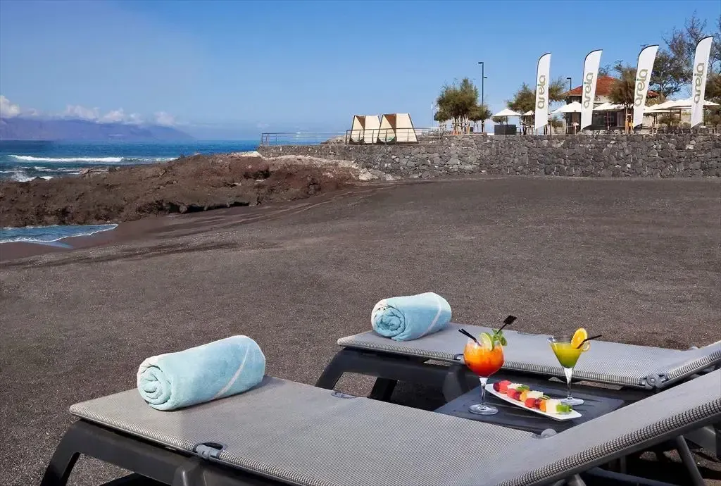 Transats avec serviettes et cocktails sur une plage de sable noir volcanique.