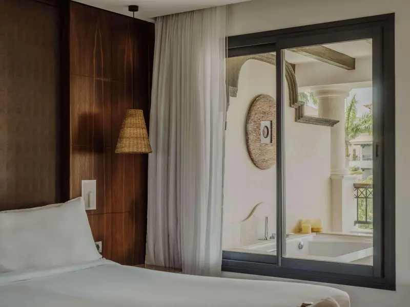 Une chambre lumineuse avec un lit blanc et une vue sur une salle de bain extérieure.