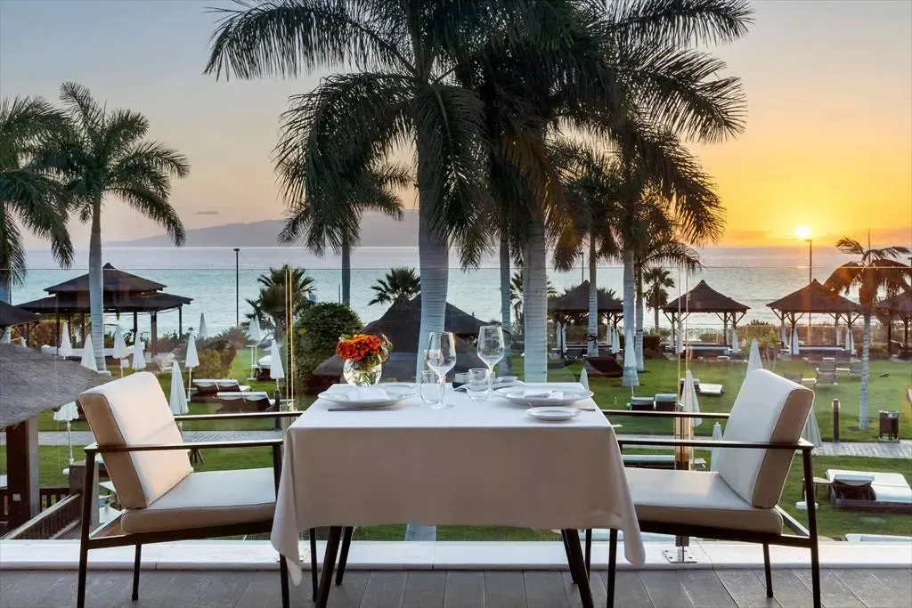 Table dressée en extérieur avec vue sur la mer au coucher du soleil.
