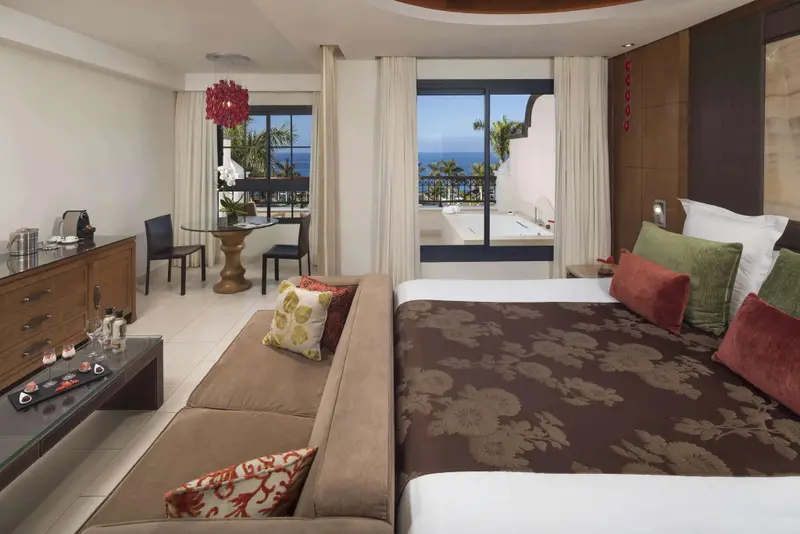 Une chambre lumineuse avec un grand lit et un coin salon donnant sur une vue mer.