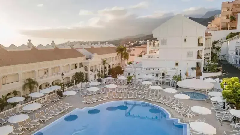 Vue aérienne d'une piscine entourée de transats blancs dans un complexe hôtelier.
