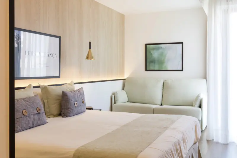 Une chambre lumineuse avec un grand lit et un canapé vert d'angle.