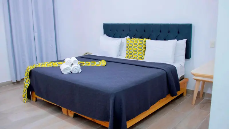 Une chambre avec un grand lit recouvert d'une couverture sombre et de coussins.