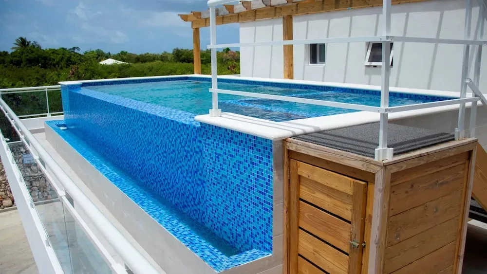 Une piscine rectangulaire à débordement avec une structure en bois au-dessus.