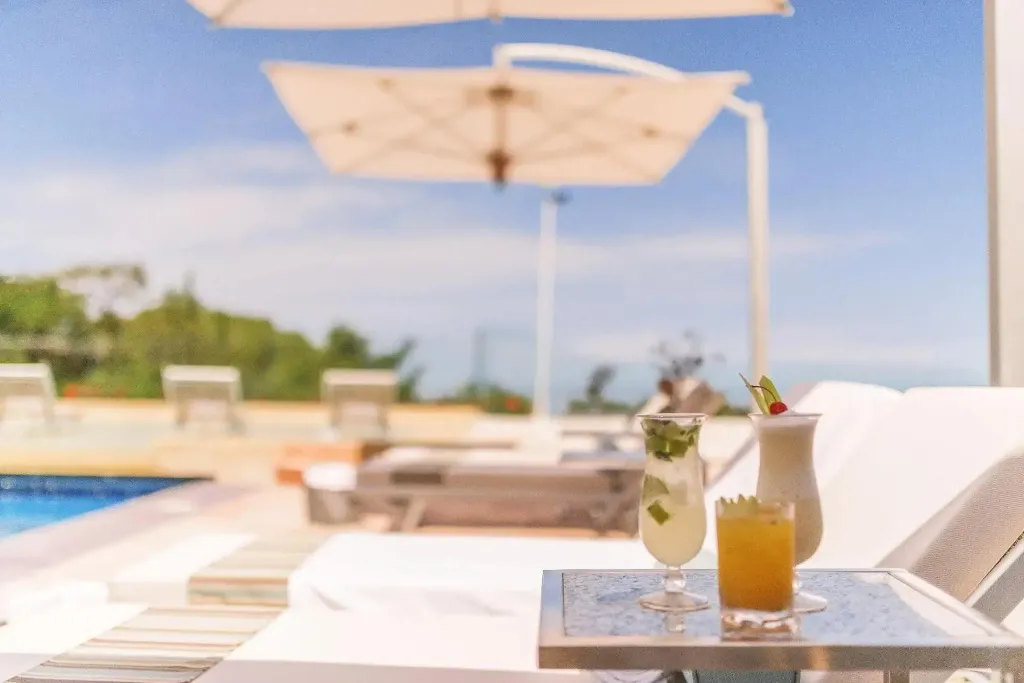 Deux cocktails colorés reposent sur une table basse au bord d'une piscine ensoleillée.